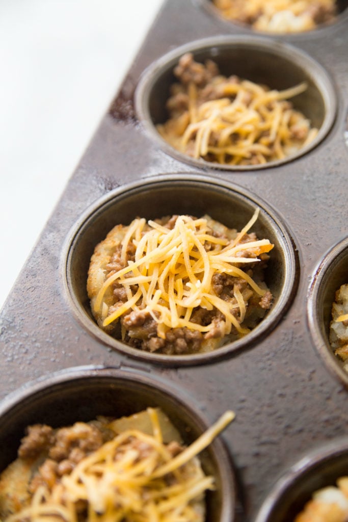Shredded cheese topping beef mixture in muffin tin