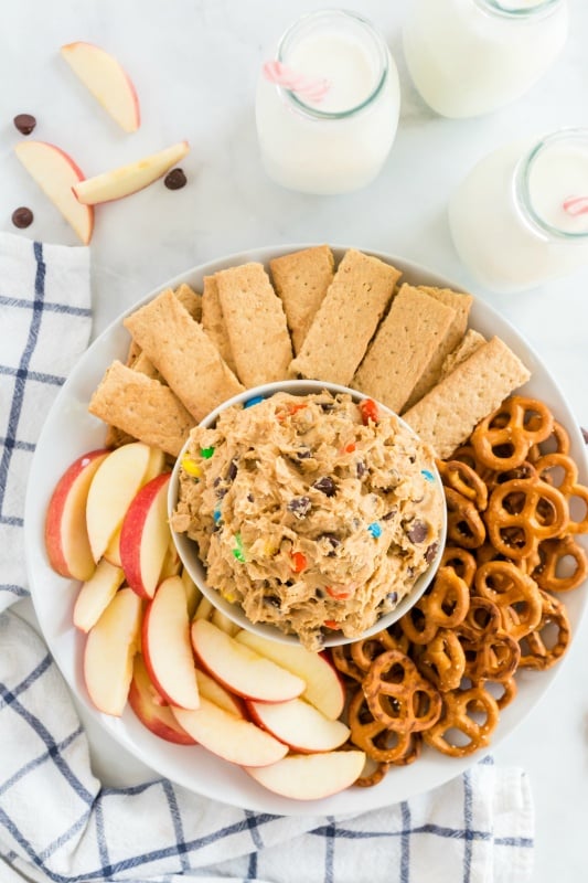 Monster Cookie Dough Dip served in a white bowl, surrounded by pretzels, sliced apples and graham crackers.