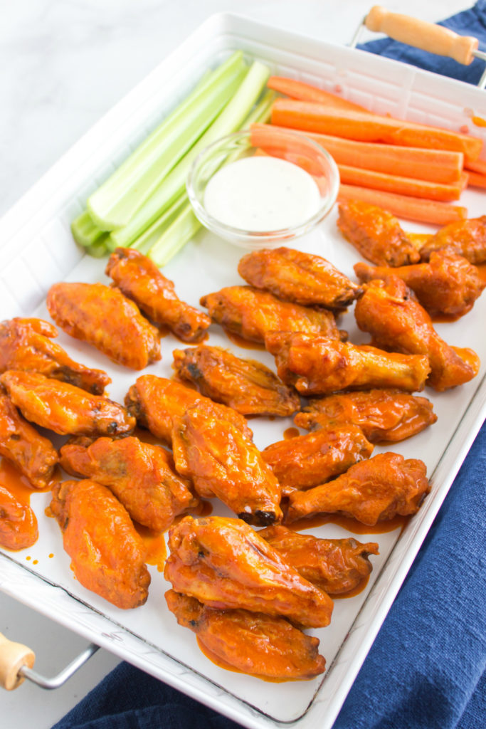  buffalo wings, celery and carrot sticks on a serving platter, with s dipping cup of dressing