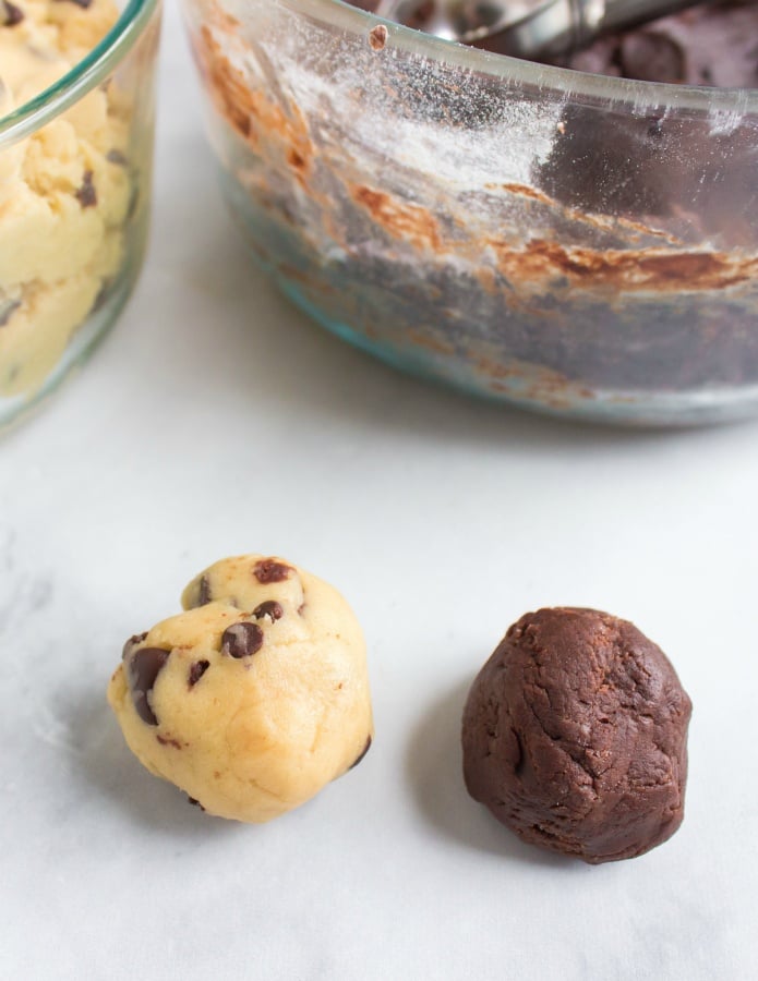 one ball of chocolate chip cookie dough and one ball of brownie batter sitting next to each other