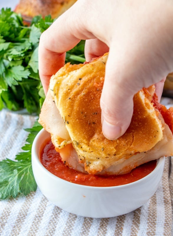 A hand holding a chicken parmesan slider, dipping it into red sauce