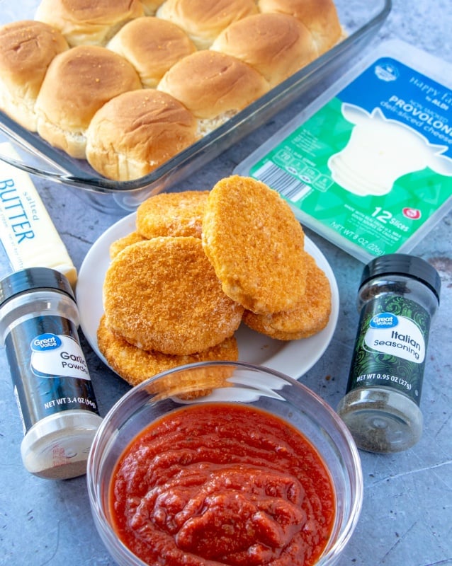 picture of ingredients for slides. Seasons containers, bowl of red sauce, plate of breaded chicken patties, package of sliced cheese and slider rolls in a baking pan