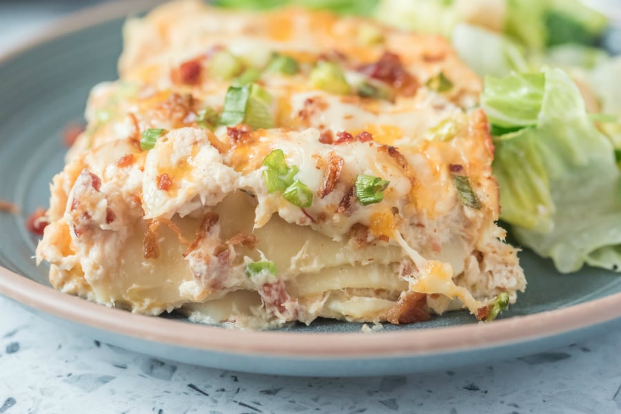 A slice of crack chicken lasagna on a blue plate with a side salad