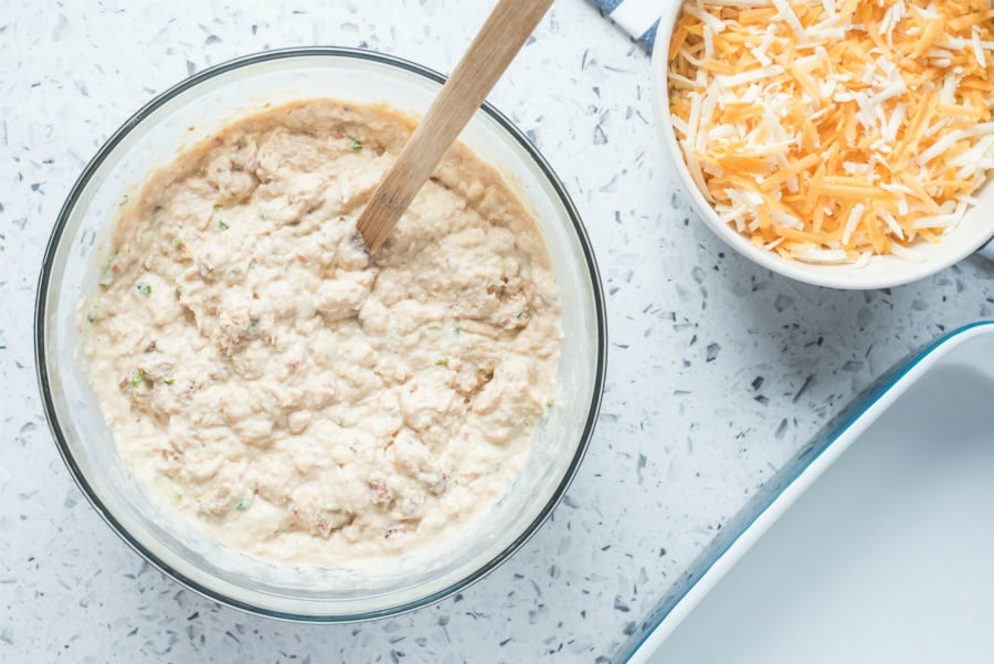 Creamy mixture in a glass mixing bow and a small bowl of shredded cheese