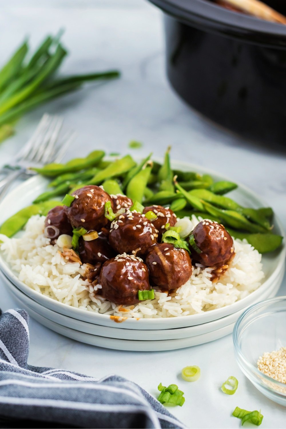 Crockpot Teriyaki Meatballs served over rice on a white plate, with a side of edamame