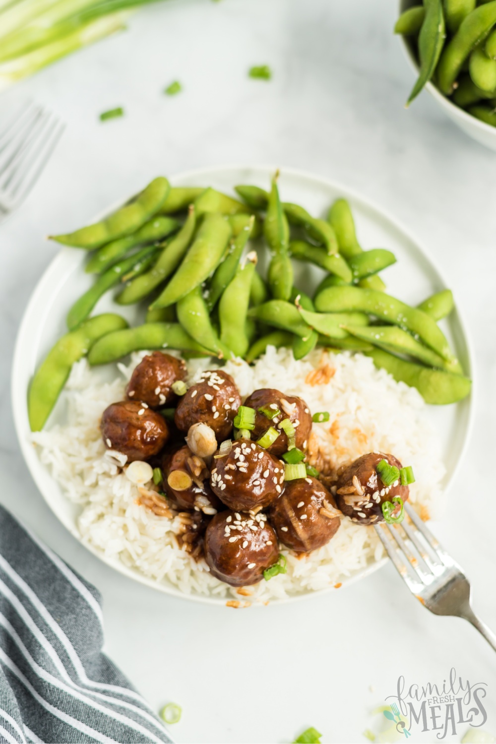 Crockpot Teriyaki Meatballs served over rice on a white plate, with edamame