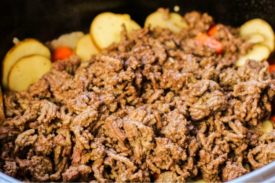 cooked ground beef being add to crockpot