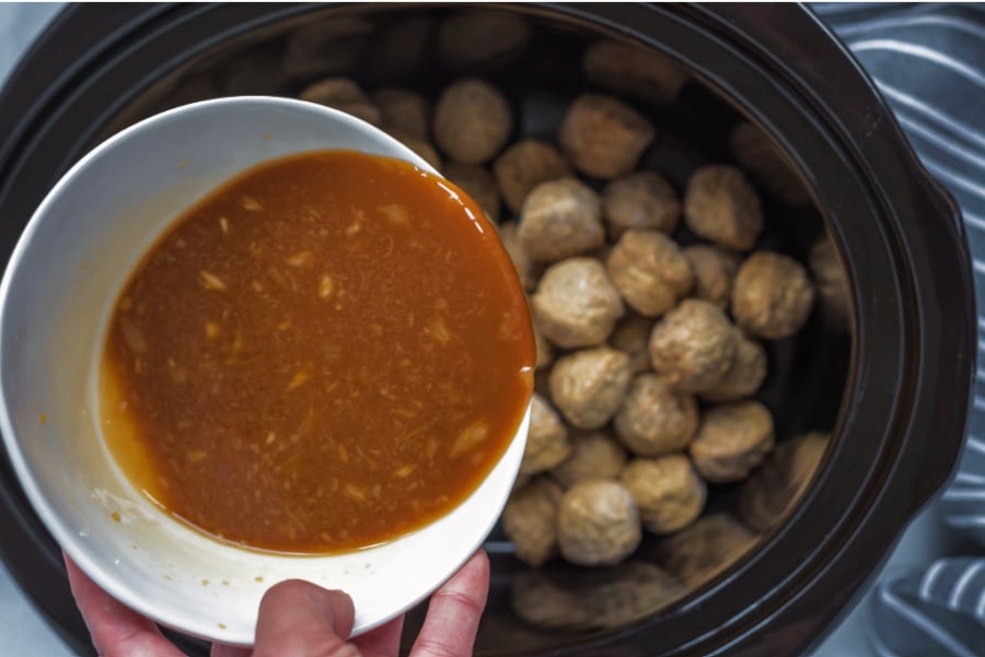 pouring brown sauce mixture over meatballs in crockpot