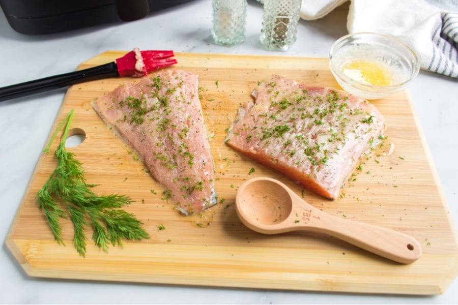 two Salmon filets on a cutting board with butter sauce brushed on