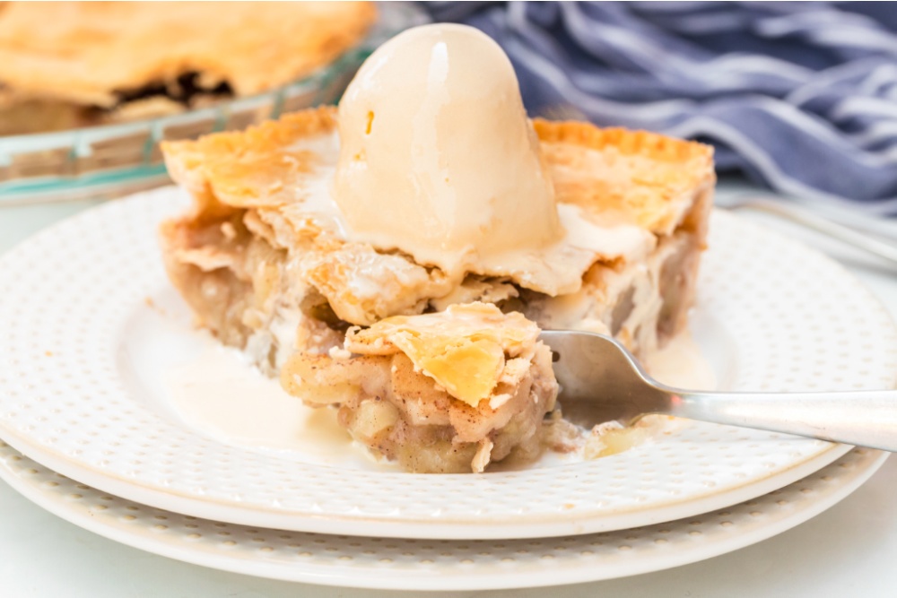 slice of apple pie on a plate with a scoop of ice cream on top and a fork cutting off a piece