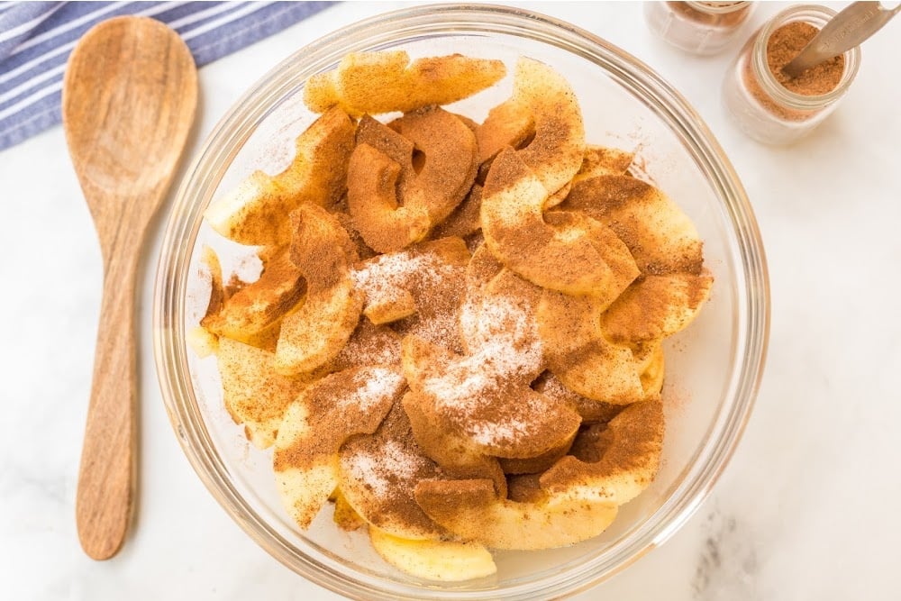 apple slices in a bowl topped with cinnamon and sugar