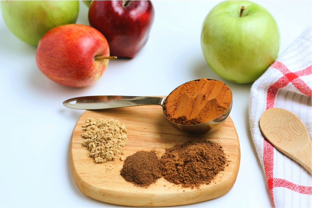 4 piles of seasoning on a small cutting board with apples in the background