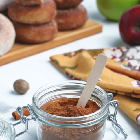 homemade apple pie spice seasoning in a small glass jar with a small wooden spoon in the jar