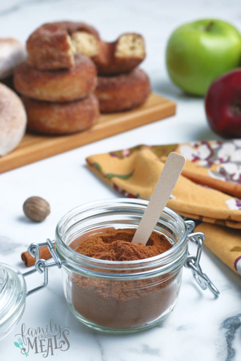 homemade apple pie spice seasoning in a small glass jar with a small wooden spoon in the jar