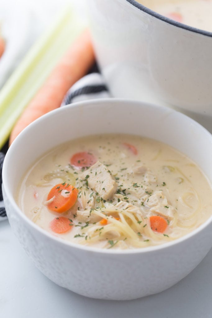 creamy chicken noodle soup in a white bowl, next to a soup pot
