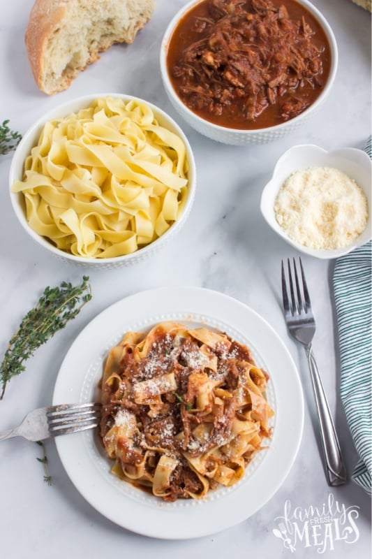 Ragu served on a plate with noodles, and bowls filled with noodles, ragu and shredded cheese