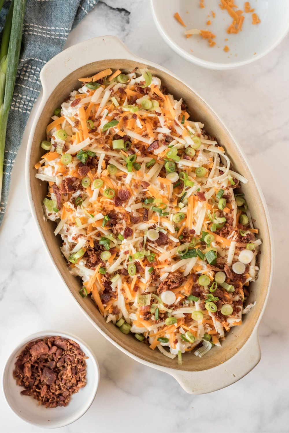 cauliflower casserole topped with shredded cheese, bacon and chives