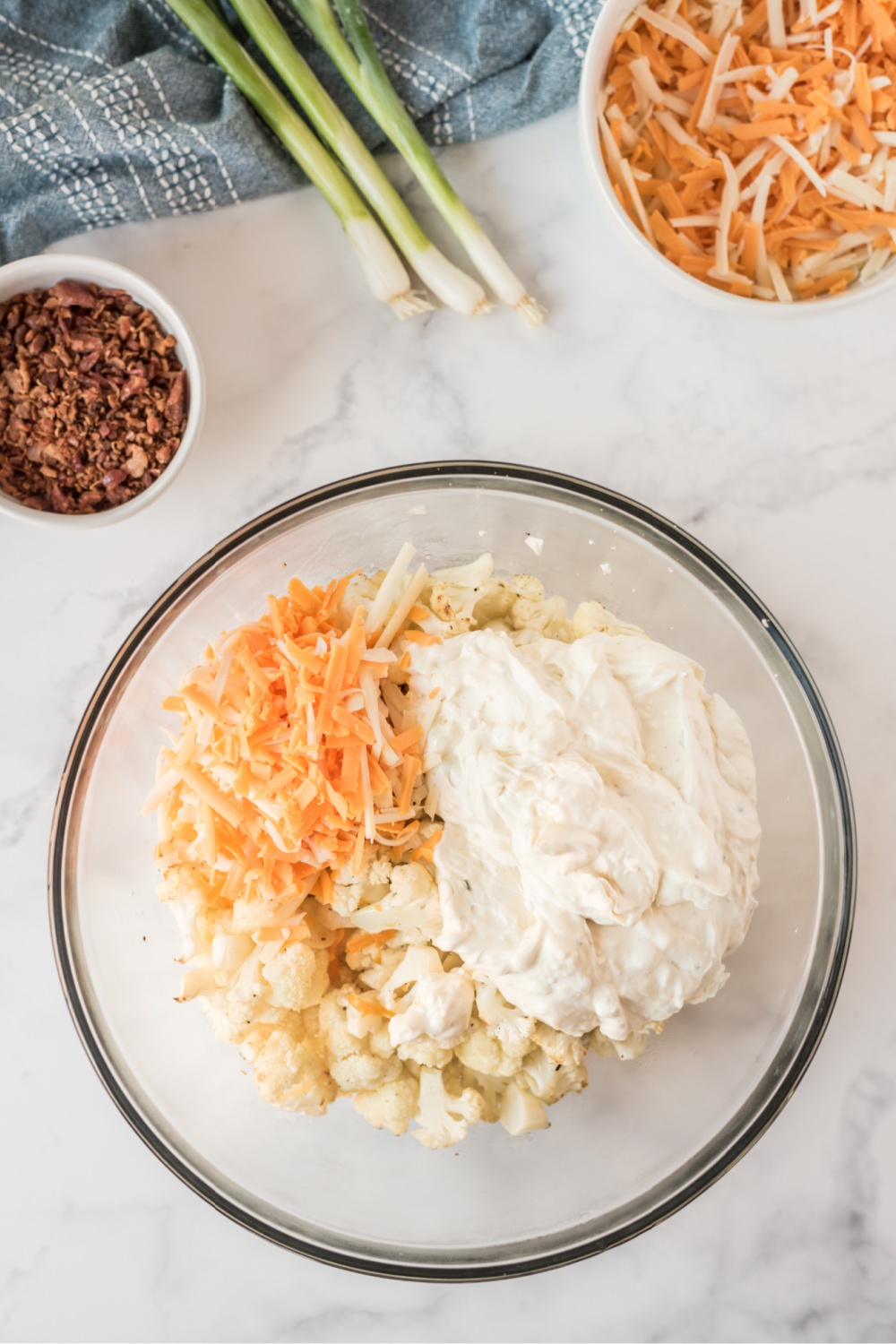 Roasted cauliflower, sauce and shredded cheese in a glass bowl