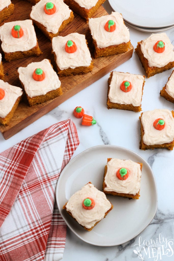 several frosted pumpkin bars on a wooden board and on a plate