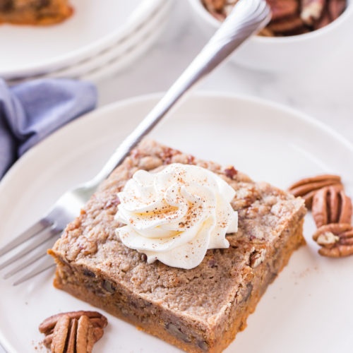 piece of dump cake on a white plate with pecans and whipped cream