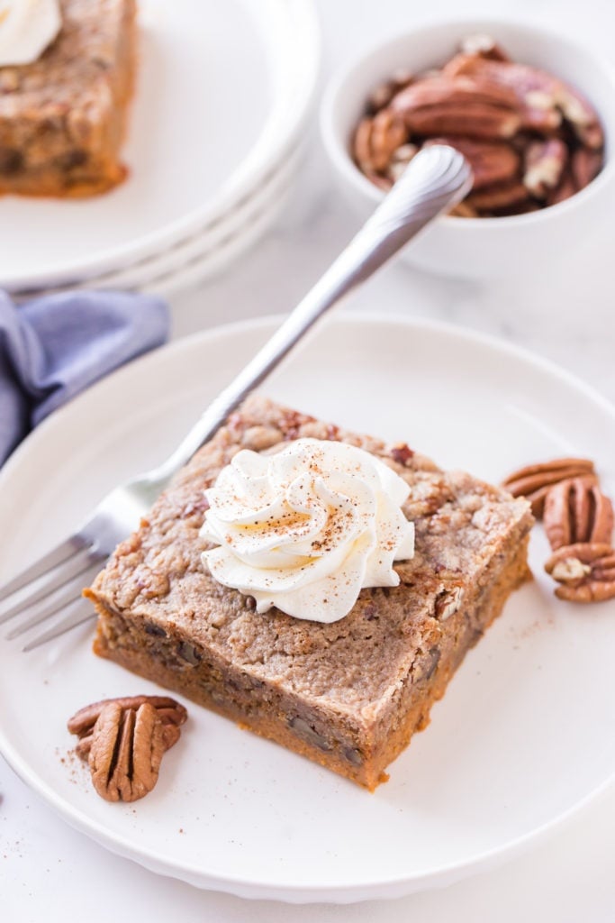 piece of dump cake on a white plate with pecans and whipped cream