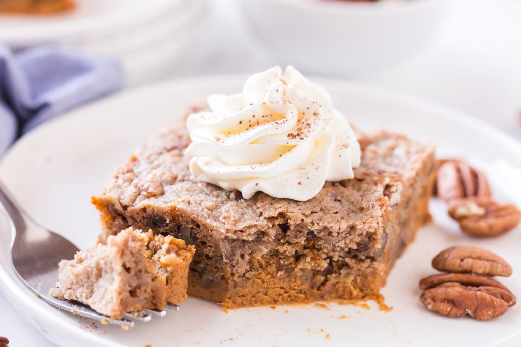 piece of pumpkin dump cake on a white plate, topped with whipped cream