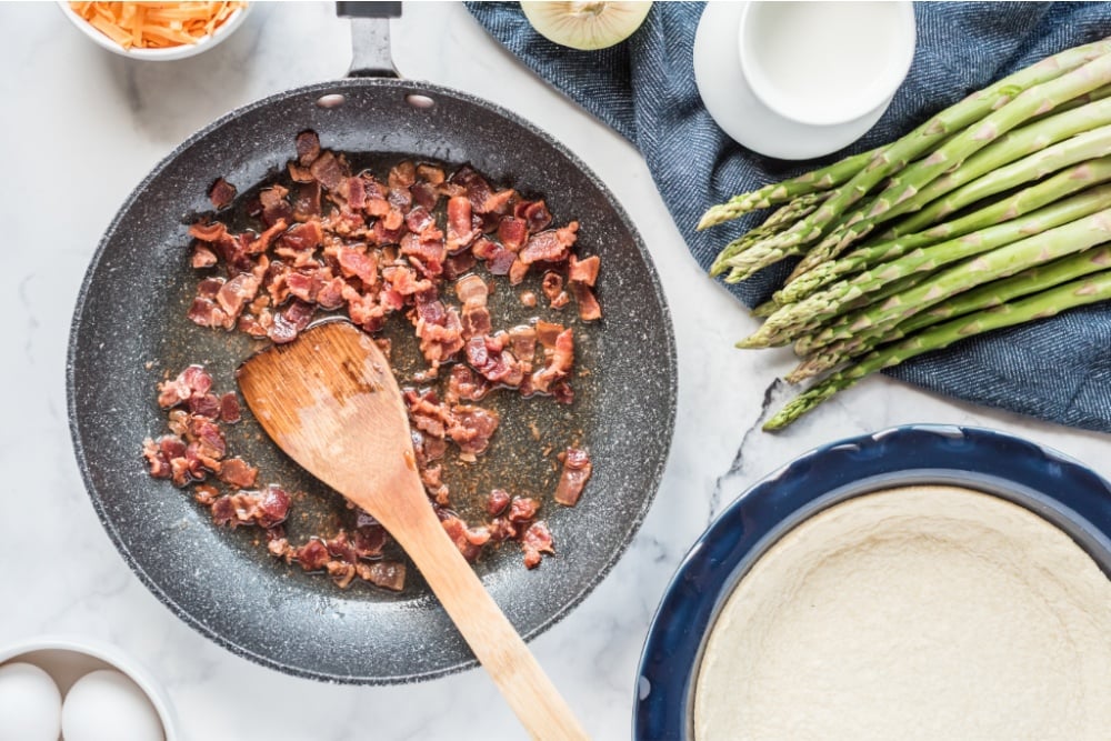 bacon cooking in a pan with a wooden spoon