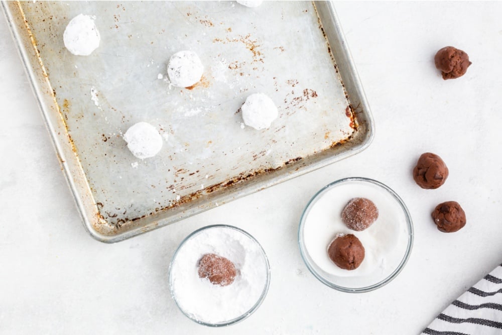 rolling cookie dough balling in sugar and powdered sugar