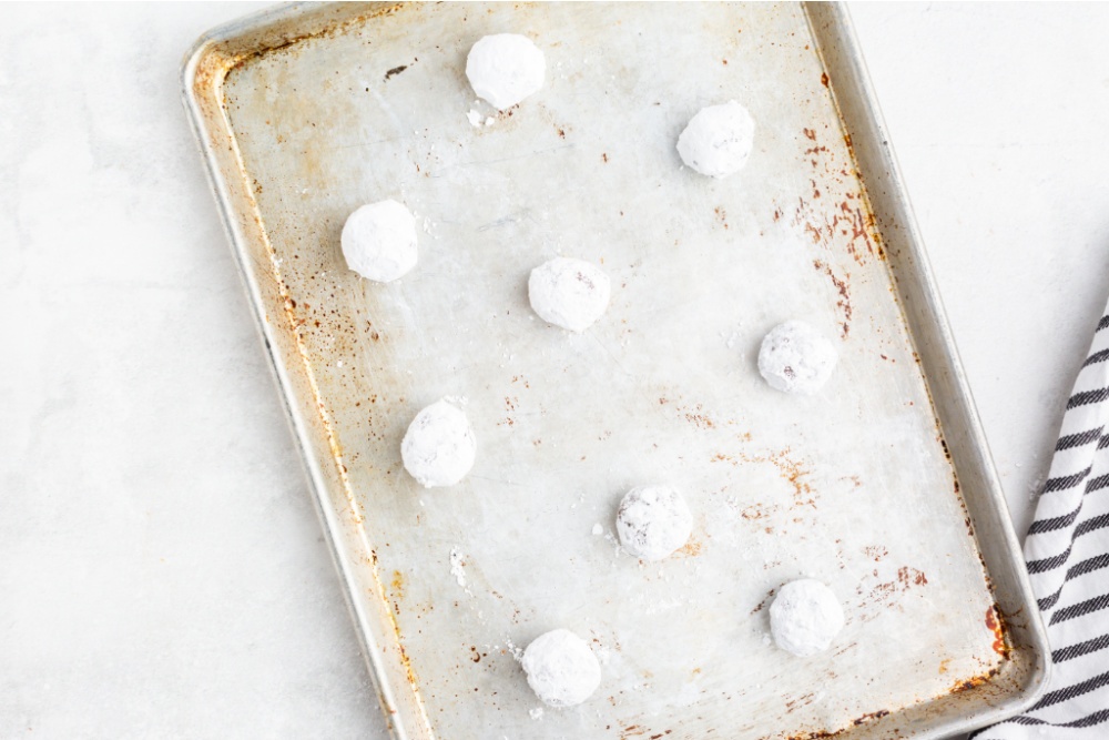 powdered sugared cookie balls on a baking sheet