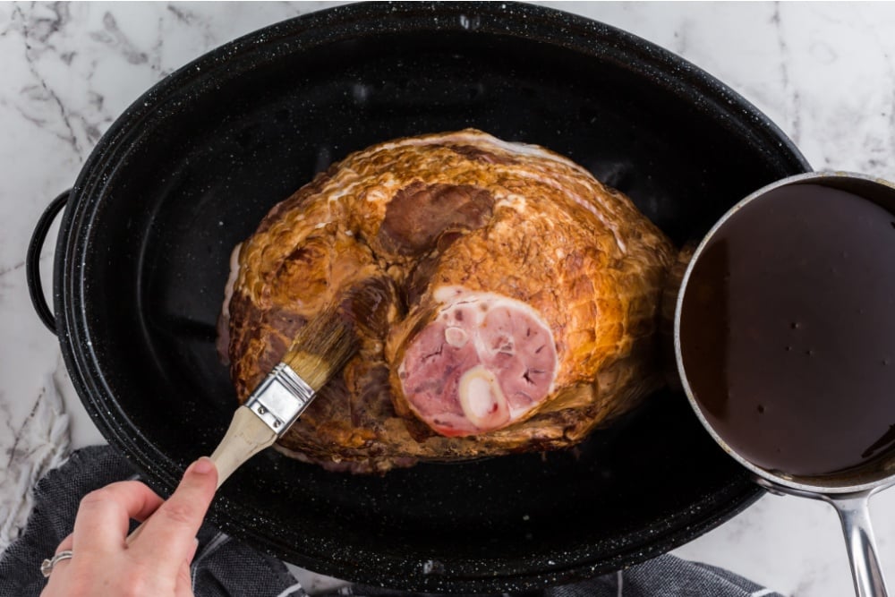 Ham in a cooking pot with a brush applying sauce to ham