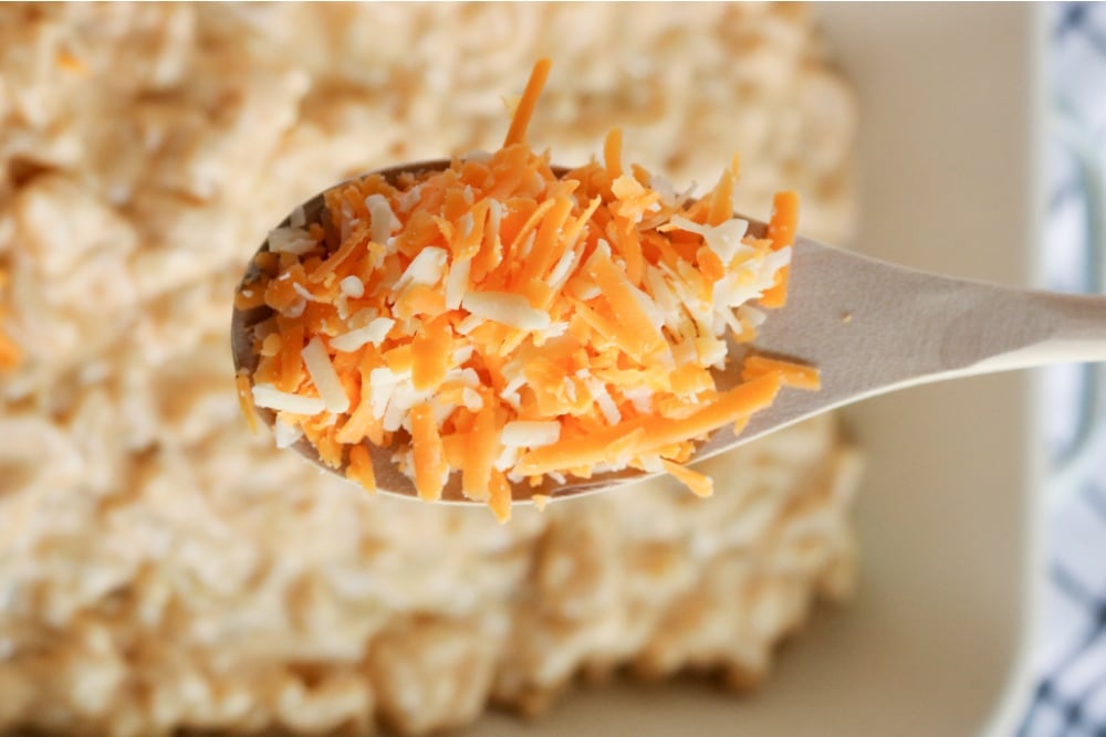 shredded cheese on a wooden spoon, held over casserole dish