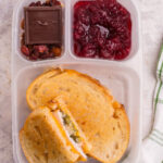 lunchbox packed with green bean casserole grilled cheese, cranberry sauce, nuts and chocolate