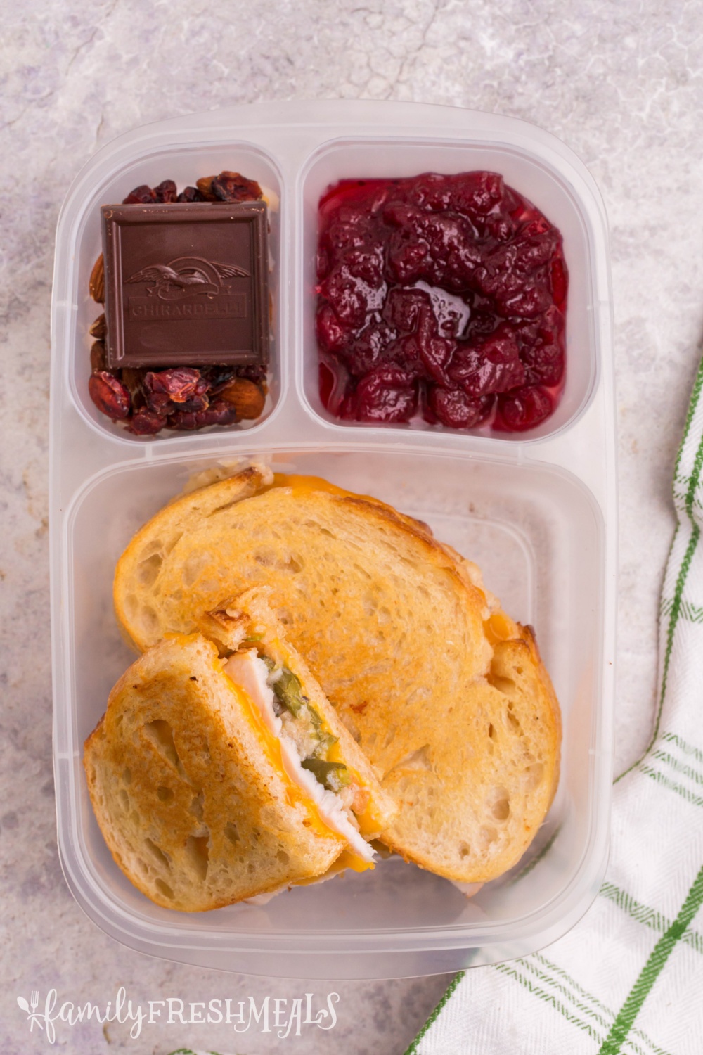 lunchbox packed with green bean casserole grilled cheese, cranberry sauce, nuts and chocolate