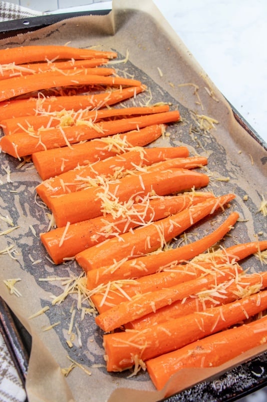 sliced carrots on baking sheet with oil, garlic and shredded cheese