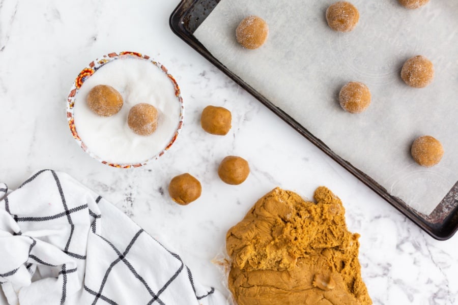 cookie balls being rolled in sugar and placed on baking sheet