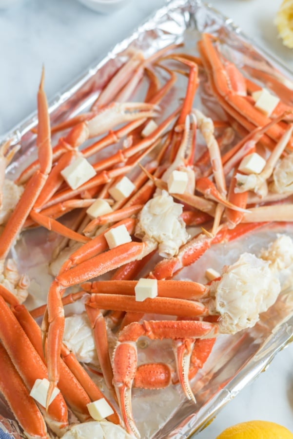 crab leg clusters on a baking sheet with butter tabs