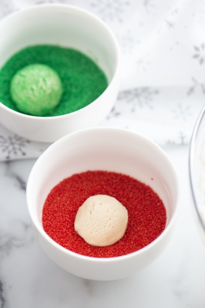 cookie balls being rolled in colored sugar sprinkles