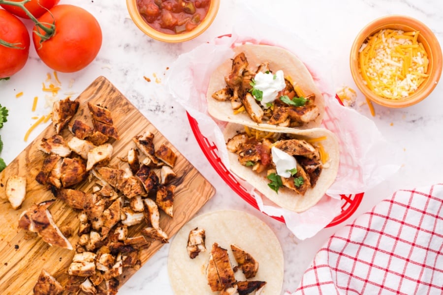 cut up chicken on a cutting board and 2 soft shell tacos in a basket