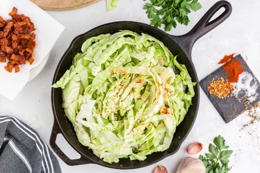 sliced cabbage and seasoning being added to pan