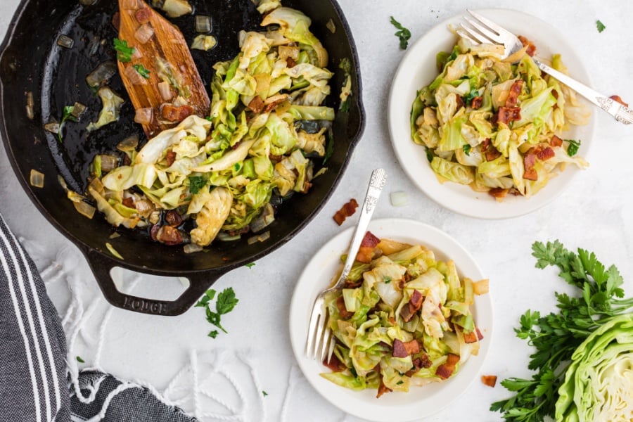 Fried cabbage and bacon in a cast iron pan and on 2 white plates