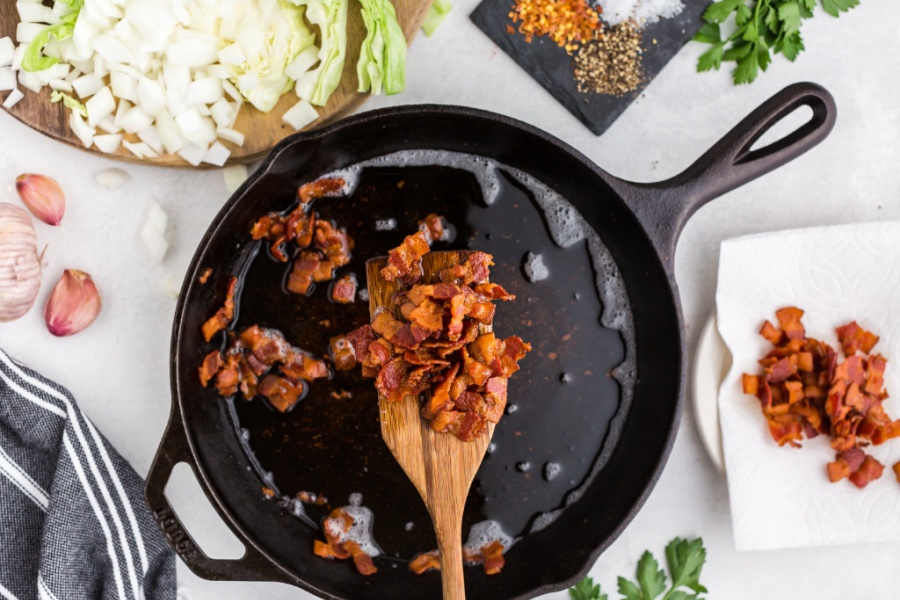 wooden spoon scooping up cooked bacon from a pan