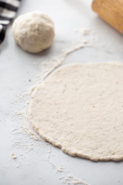 pizza dough rolled out on floured surface