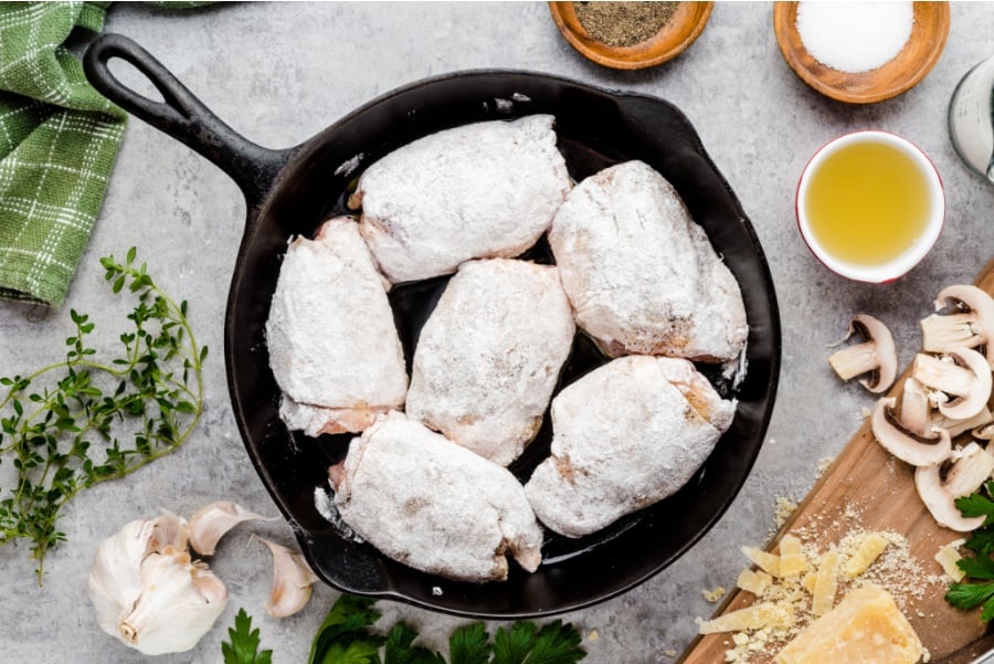 flour coated chicken thighs in cast iron skillet