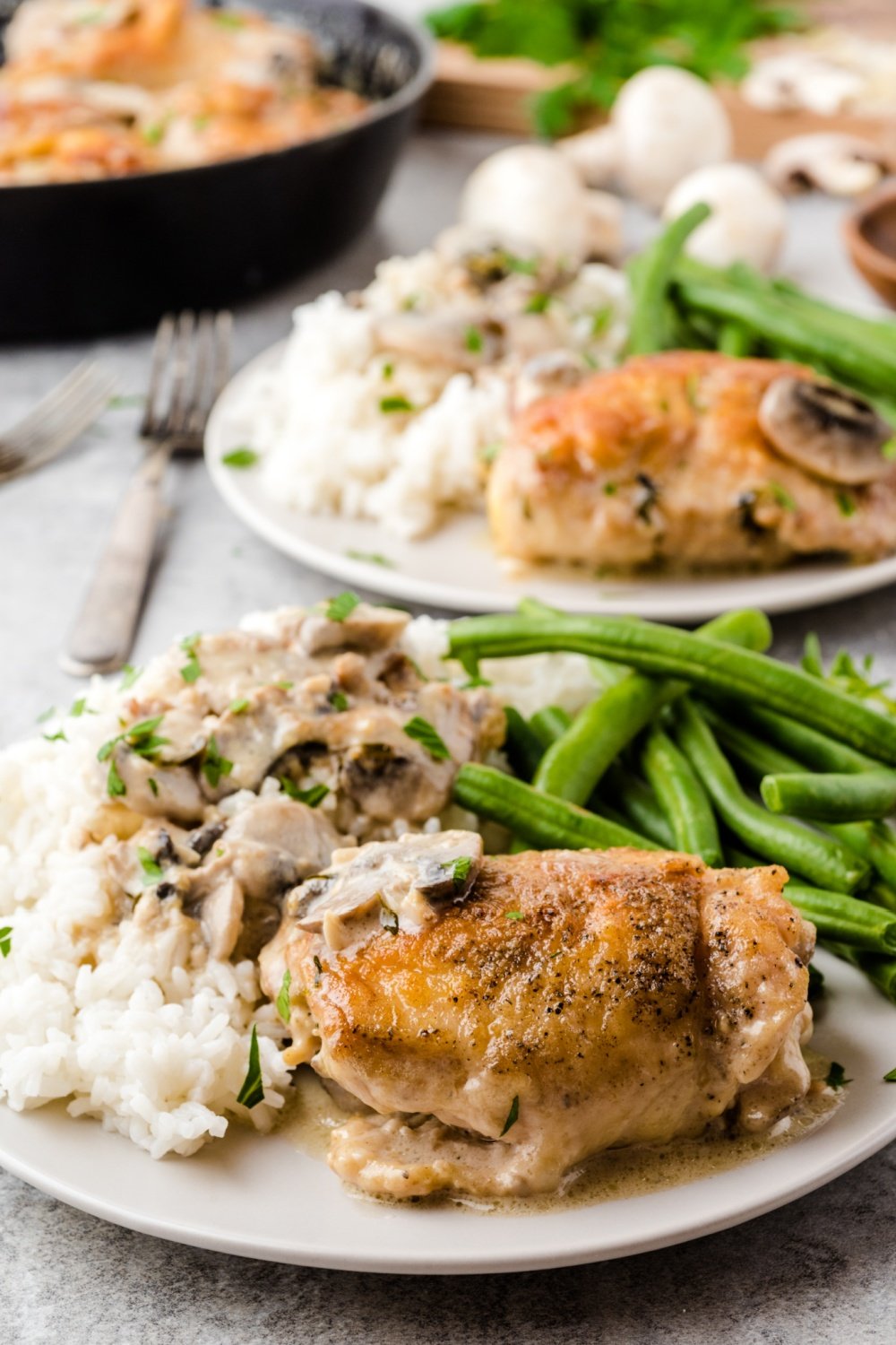 Chicken thighs served with rice and green beans on 2 plates