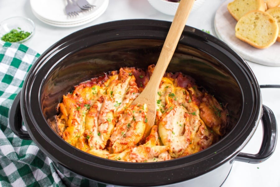 Stuffed shells in a crockpot with a wooden spoon