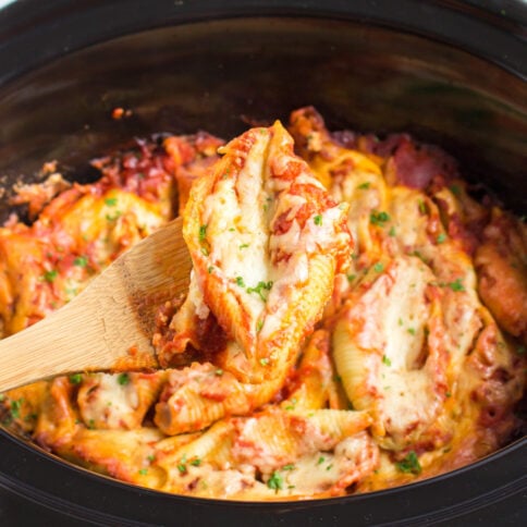 Crockpot Stuffed Shells in a slow cooker with a wooden spoon scooping up a serving