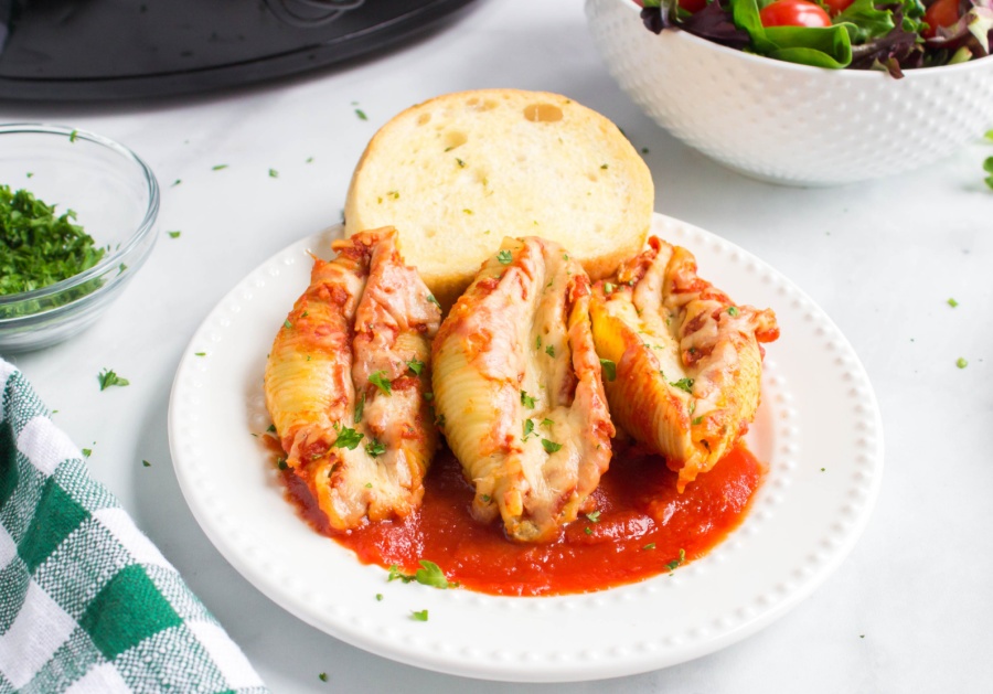 3 stuffed shells on a plate with a piece of bread
