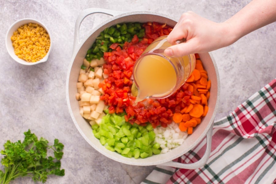 ingredients for soup in a large soup pot with a hand pouring in broth