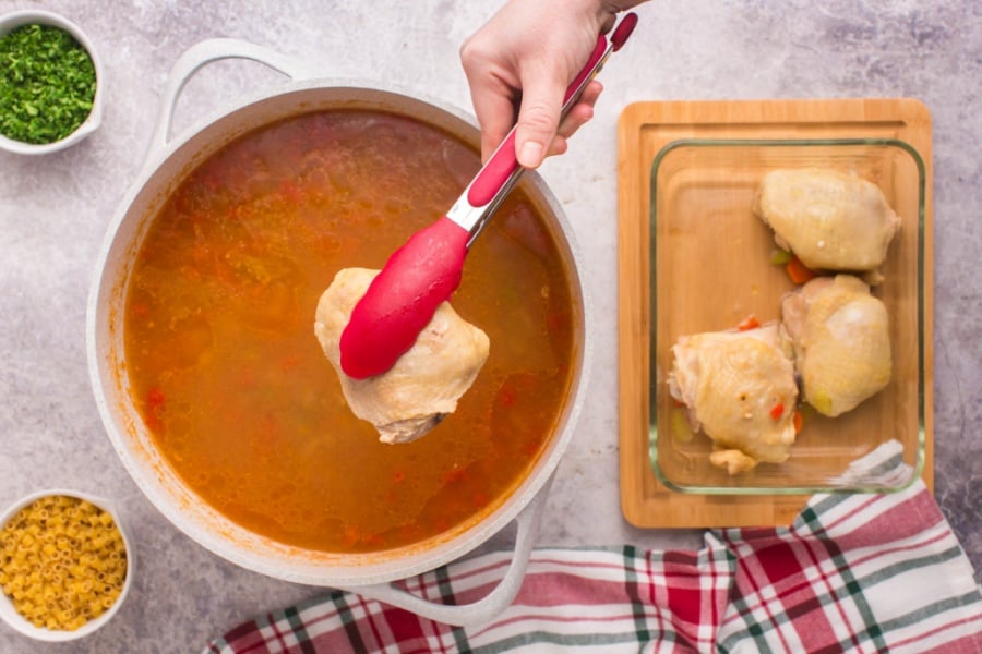 removing chicken with tongs from soup pot