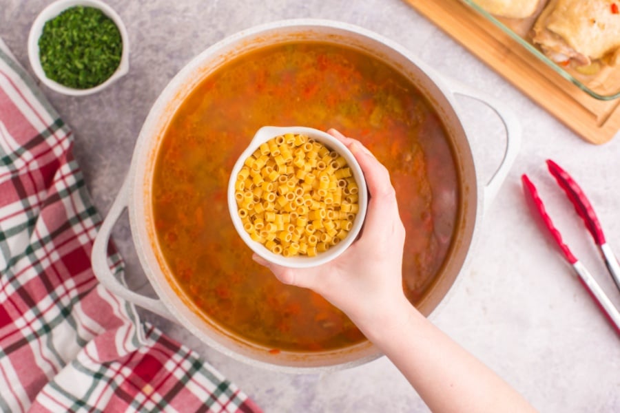 holding a cup of pasta over soup pot